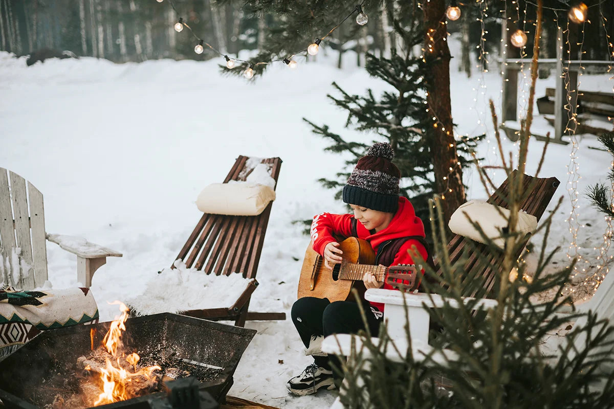 Caucasian boy playing guitar outside by a fire during the holiday season