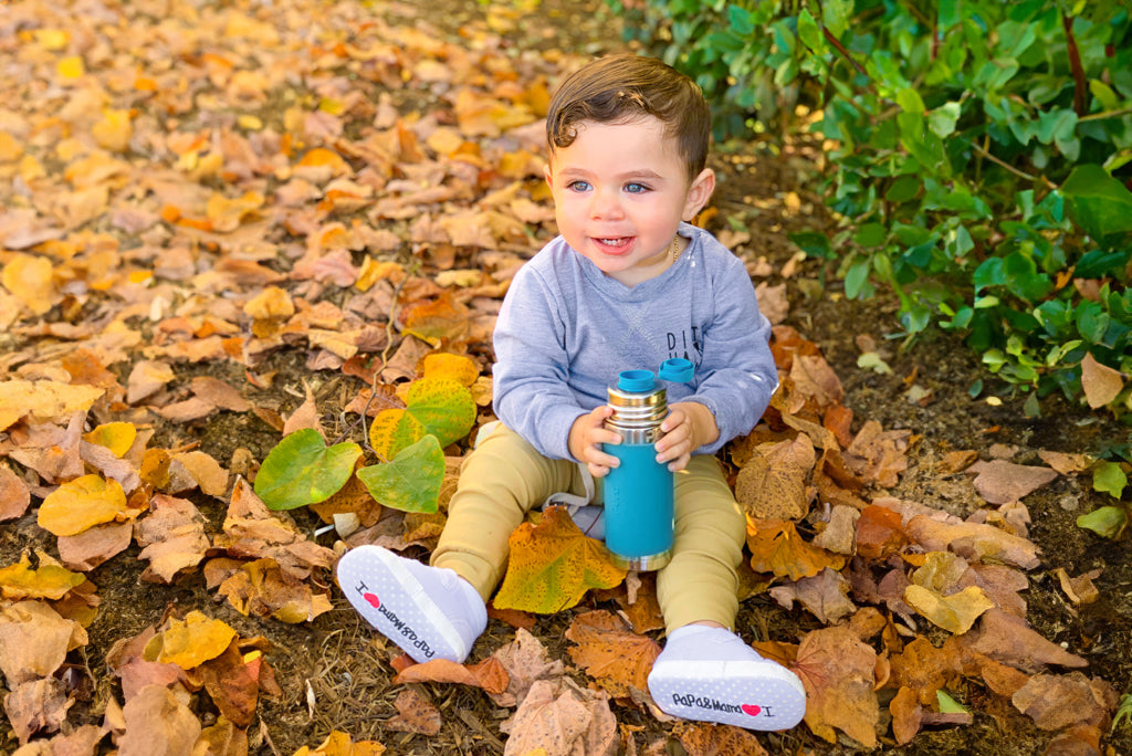 Toddler sitting outdoors with a Kiki stainless steel bottle with a Big Mouth lid.